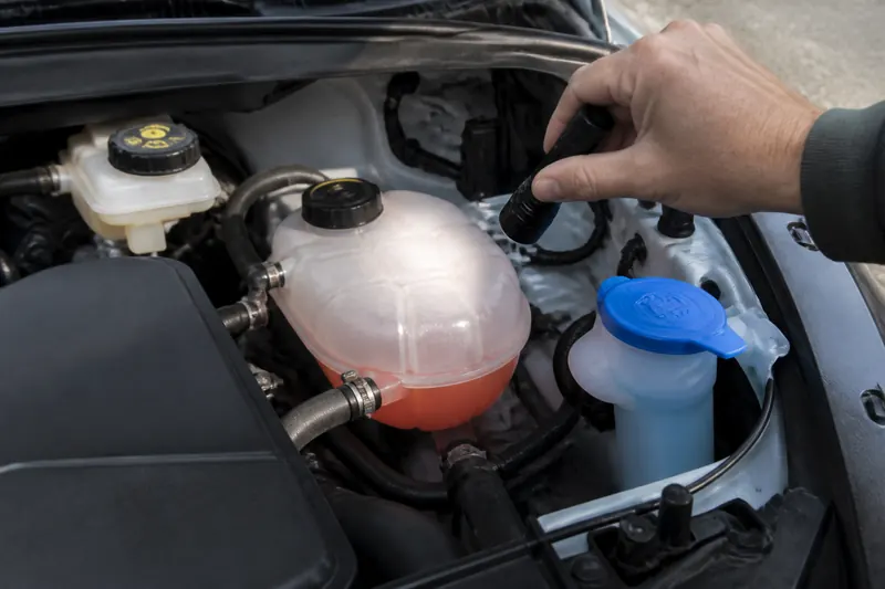 Checking the coolant level with a flashlight beside the washer fluid reservoir