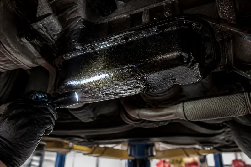 A flashlight on an oily oil pan under a car on a lift