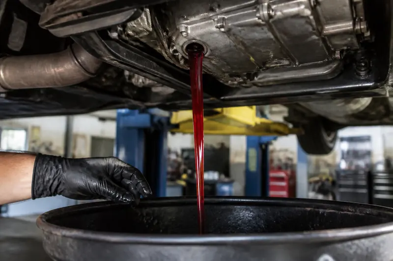 Red transmission fluid draining into a drain pan under a car on a lift