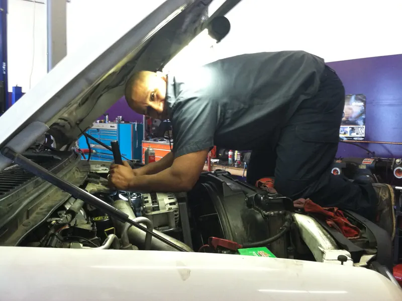 Carlos leaning into the engine bay of a white vehicle