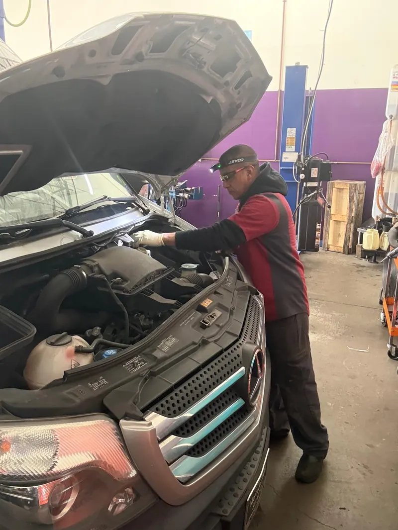 Carlos working under the open hood of a vehicle in the shop