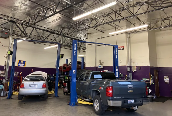 Two service bays with lifts inside Ali's Woodinville Auto Repair, a sedan and a pickup being worked on