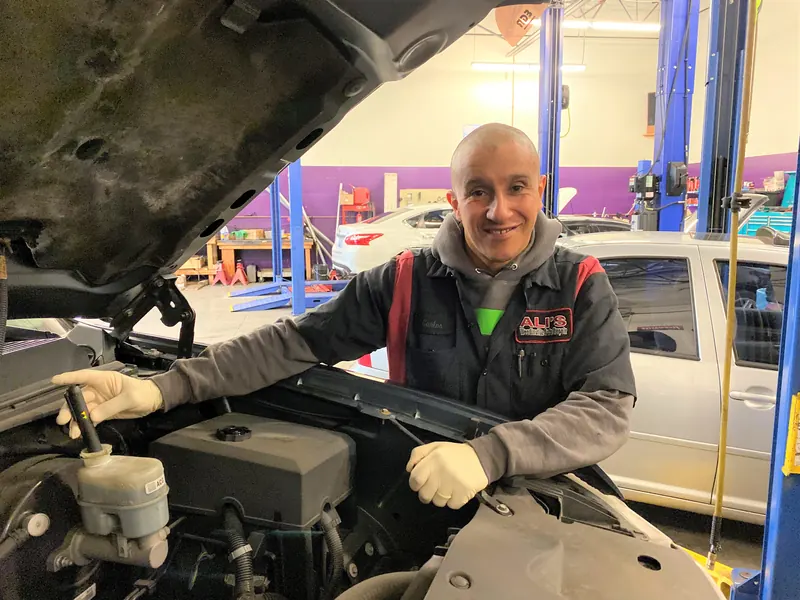 A technician smiling from under the hood of a car in the service bay