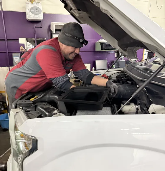 Luis leaning under the hood of a white pickup in the shop
